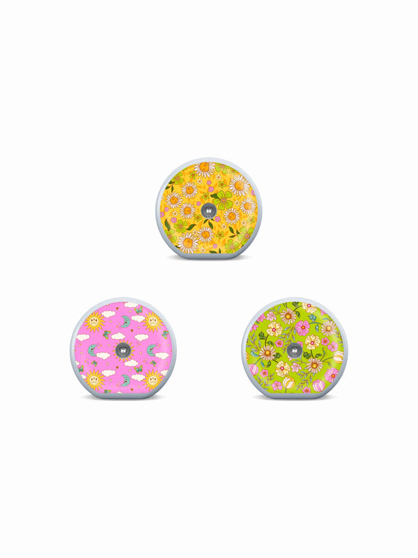 Three Accu-Chek SmartGuide sensor stickers with daisies, sun and moon motifs, and bright floral summer patterns.